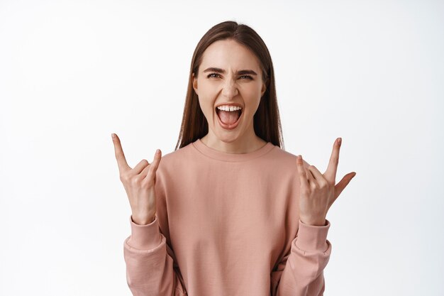 woman enjoying event, concert and party, shouting with joy and excitement, shaking rock on heavy metal horns, having fun on white