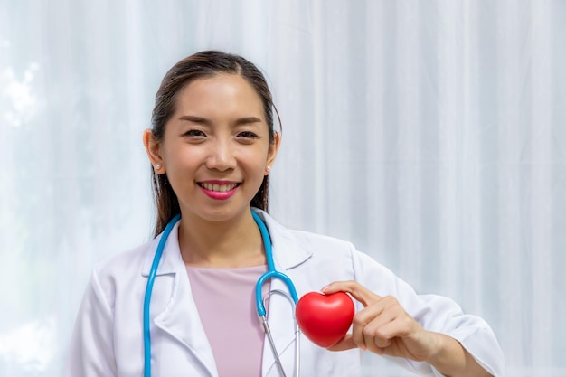 Foto gratuita medico femminile della donna che tiene il cuore rosso in mano e diagnostica con lo stetoscopio