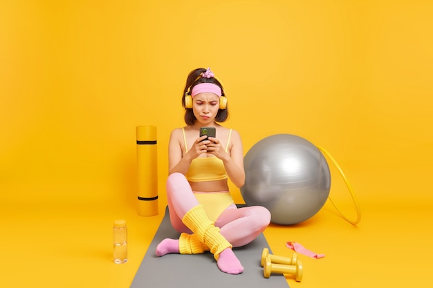 Бесплатное фото Женщина, сосредоточенная на дисплее смартфона, использует спортивное снаряжение, одетое в спортивную одежду