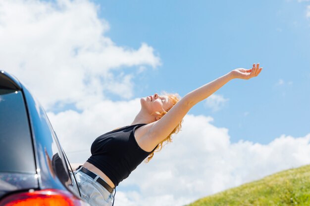 Женщина поднимает руку к небу из окна автомобиля в солнечный день