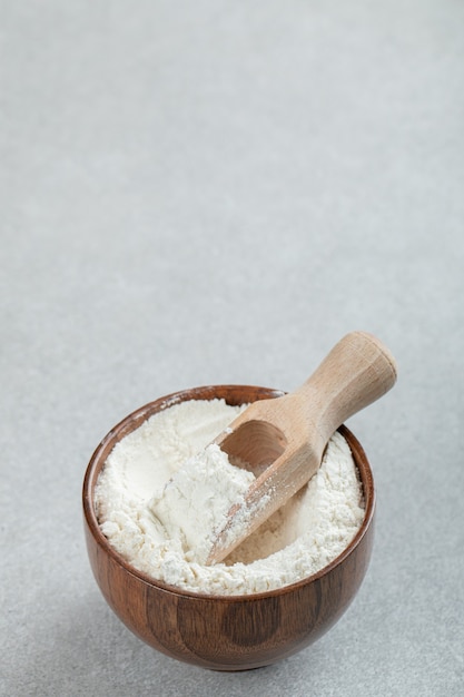Free photo a wooden bowl of flour and wooden spoon on marble surface.