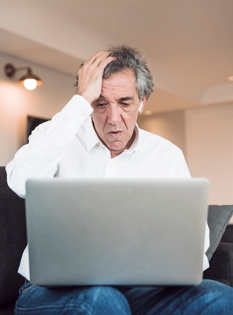 Worried senior man sitting on sofa looking at laptop