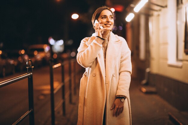 Молодая женщина с помощью телефона на улице ночью