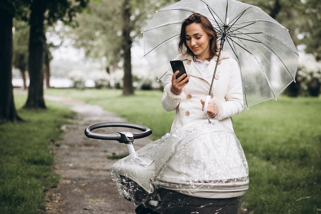 Бесплатное фото Молодая женщина гуляет с коляской под зонтиком в дождливую погоду