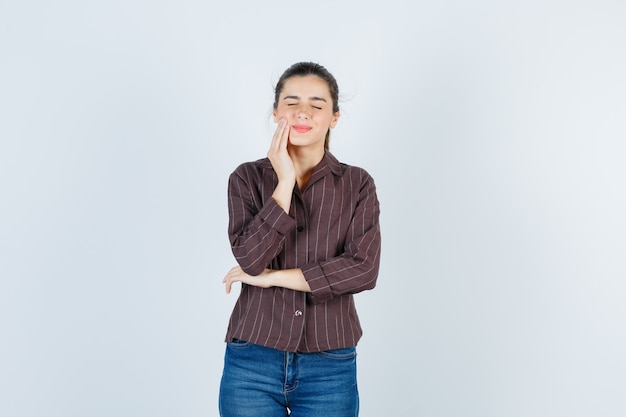 Free photo young woman with hand near mouth, having toothache in striped shirt, jeans and looking exhausted. front view.