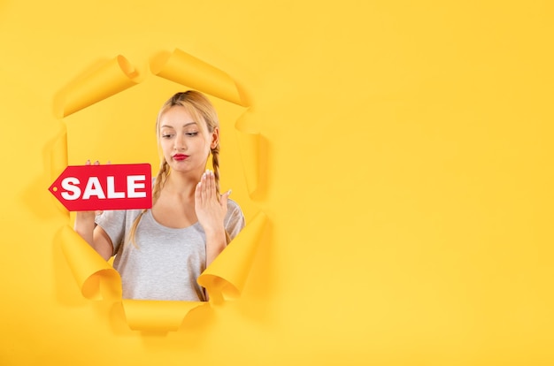 Бесплатное фото Молодая женщина с надписью продажи знак на порванной желтой бумажной поверхности лица закрытые покупки