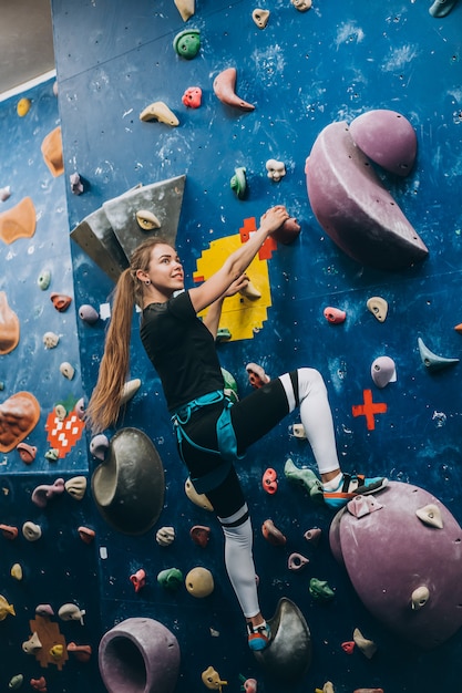 Молодая женщина, взбирающаяся на высокую крытую искусственную скалолазную стену