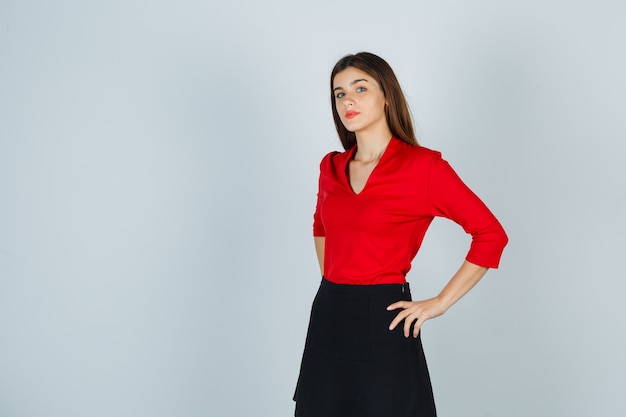 Free photo young woman holding hands on hips in red blouse, black skirt and looking confident