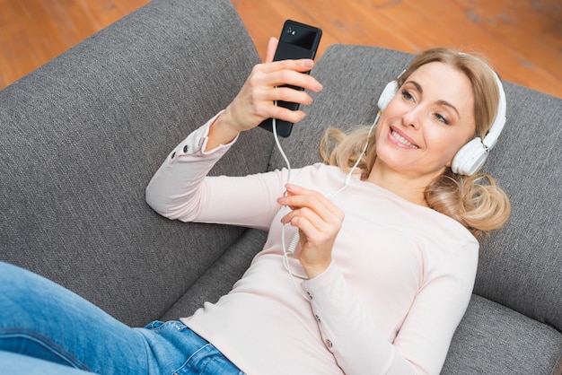 Young woman lying on sofa listening to the music with headphone from a smart phone