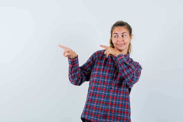 Free photo young woman pointing left with index fingers in checked shirt and looking pretty