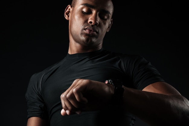 Young african muscular man looking at watch