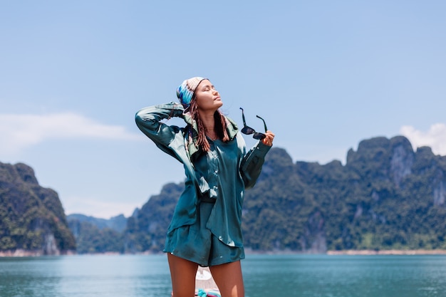 Бесплатное фото Молодой азиатский счастливый турист блоггера женщины в шелковом костюме и шарфе и солнечных очках на каникулах путешествует вокруг таиланда на азиатской лодке, национальном парке khao sok.