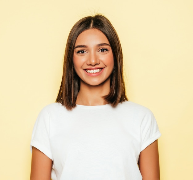 Free photo young beautiful woman looking at camera. trendy girl in casual summer white t-shirt and jeans shorts. positive female shows facial emotions. funny model isolated on yellow