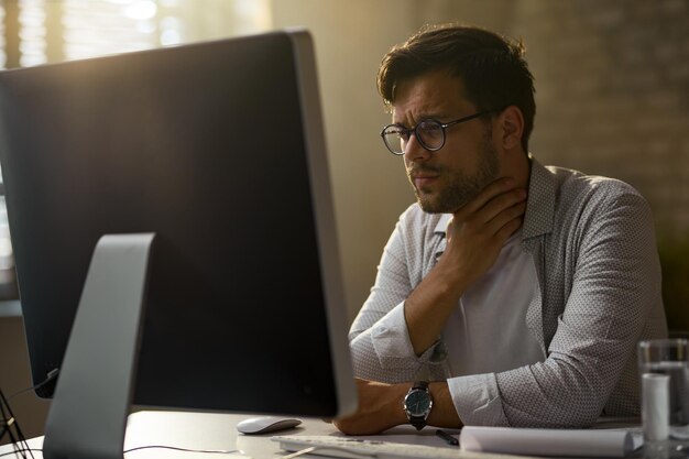 Young businessman feeling pain in his throat while working on desktop PC in the office