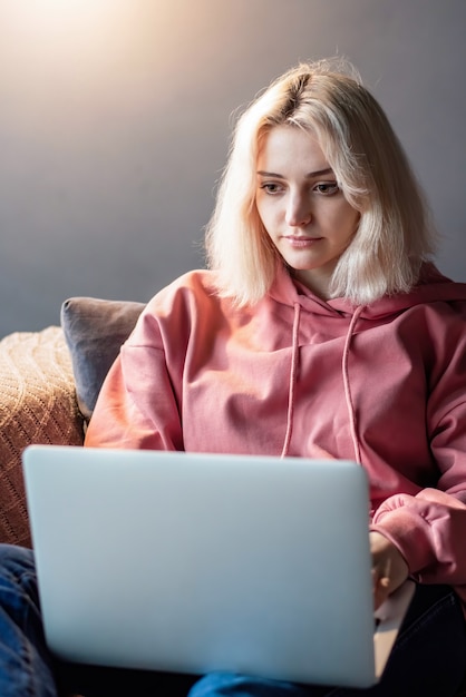 Бесплатное фото Молодая блондинка создатель контента сидит на своем ноутбуке на диване. работать из дома