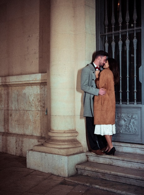 Молодая пара целуется, опираясь на стену здания