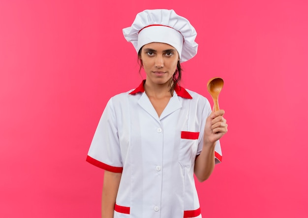 Бесплатное фото Молодая женщина-повар в униформе шеф-повара держит ложку на изолированной розовой стене с копией пространства