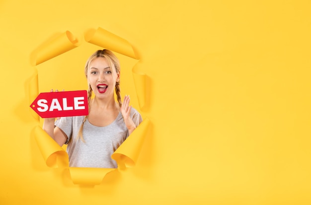 Бесплатное фото Молодая женщина с табличкой продажи на фоне рваной желтой бумаги делает покупки в помещении