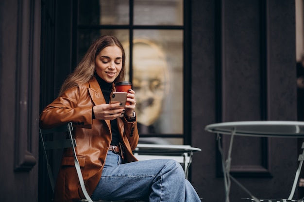 Бесплатное фото Молодая девушка сидит возле кафе и пьет кофе