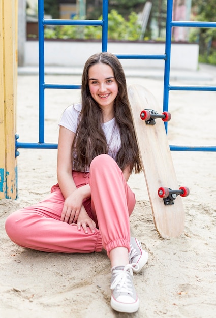 Free photo young girl sitting next to skateboard outside