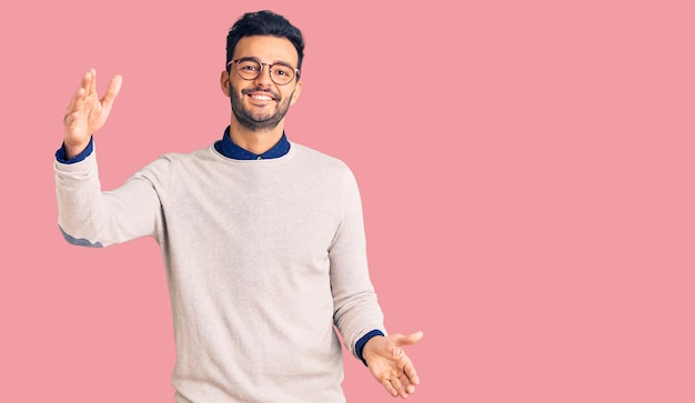 Free photo young handsome hispanic man wearing elegant clothes and glasses looking at the camera smiling with open arms for hug cheerful expression embracing happiness