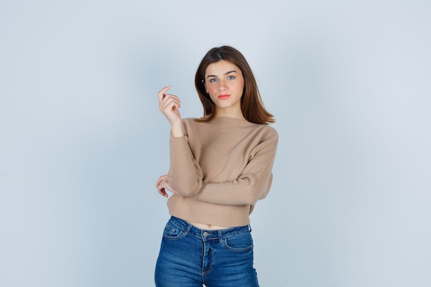 Free photo young lady in beige sweater, jeans posing while looking at front and looking confident , front view.