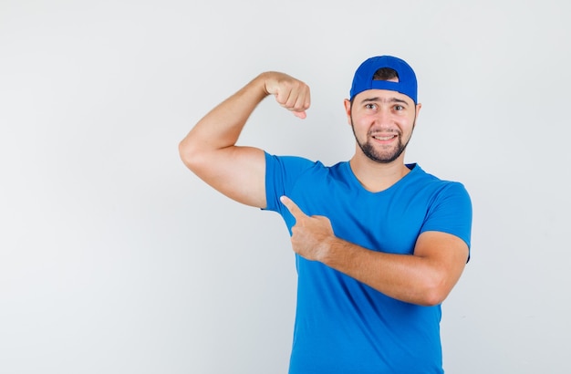 Free photo young man in blue t-shirt and cap pointing at his muscles and looking confident