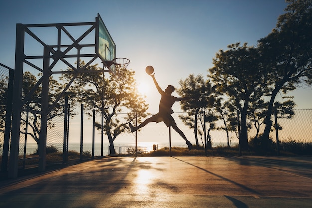 Free photo young man doing sports, playing basketball on sunrise, jumping silhouette