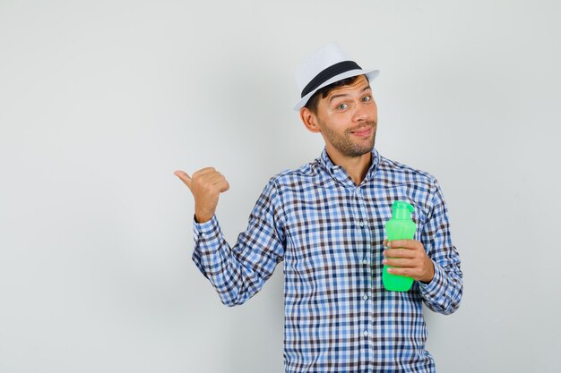 Free photo young man holding bottle for water, pointing away in checked shirt