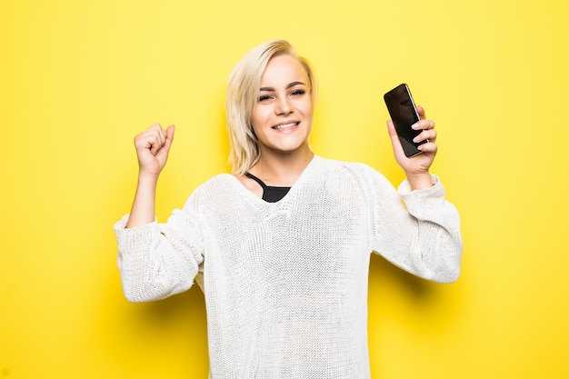 Free photo young pretty lady woman girl in white sweater uses smartphone on yellow