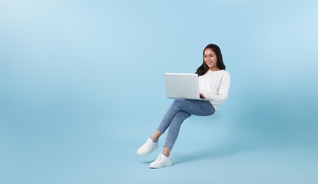 Foto gratuita giovane studentessa asiatica sorridente che galleggia a mezz'aria con l'utilizzo del computer portatile