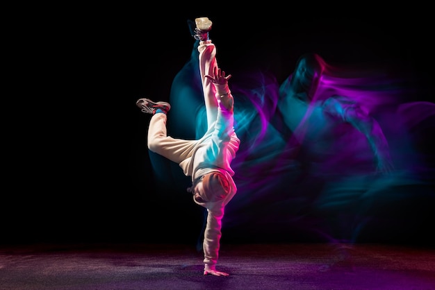 Free photo young sportive man daancing breakdance isolared over black backgrounf in neon with mixed lights