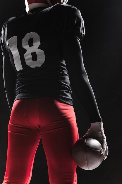 Free photo american football player posing with ball on black background