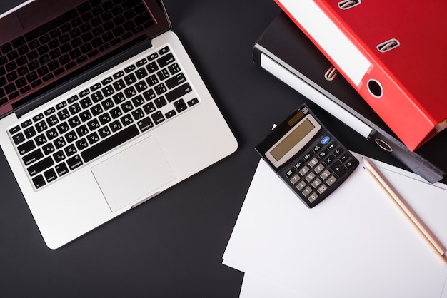 Бесплатное фото Верхний вид ноутбука; файловые папки; калькулятор; карандаши и бумага на черном фоне