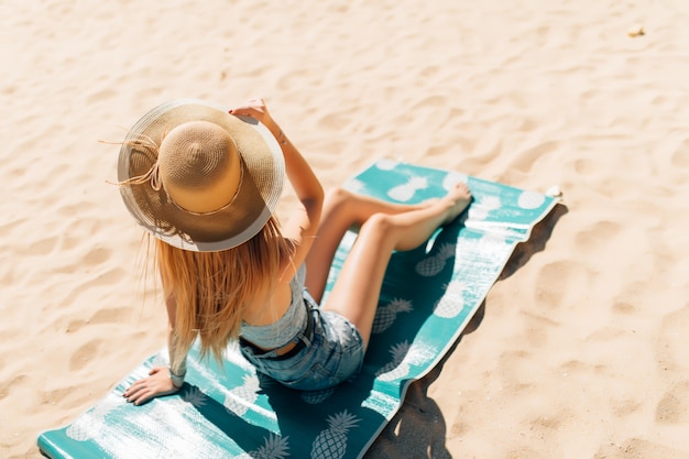 Бесплатное фото Привлекательная девушка в солнцезащитных очках и шляпе лежит на теплом песке