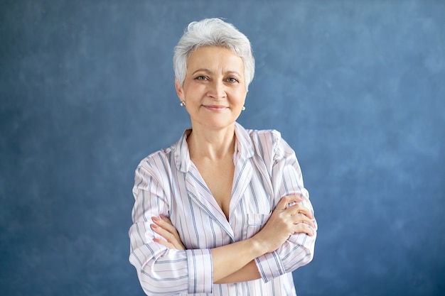 Free photo attractive retired female with short gray hair posing with confident smile crossing arms on her chest