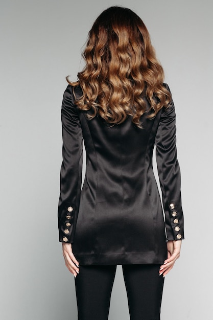Free photo back view of unrecognizable model with brunette wavy hair of medium length wearing casual black jacket and trousers made from silk isolate on grey studio shot