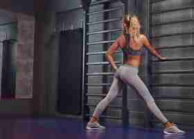 Бесплатное фото Красивая фитнес-женщина делает растяжку, опираясь на шведскую стенку в современном фитнес-центре.