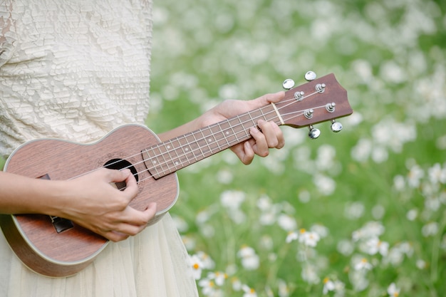 Красивая женщина в милом белом платье и держит гавайскую гитару