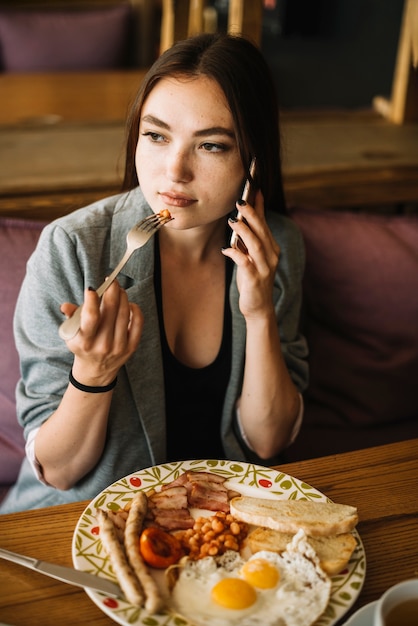 Free photo beautiful young woman talking on mobile phone eating food with fork