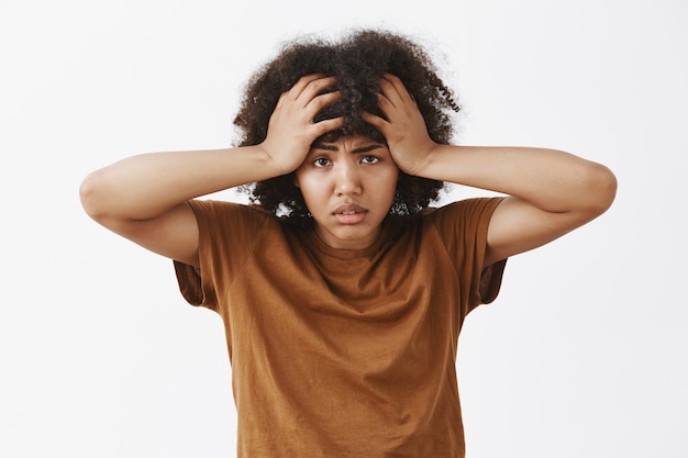 Free photo bothered and tired depressed african american woman with afro hairstyle feeling annoyed and exhausted with louds of troubles on head frowning holding hands on hair
