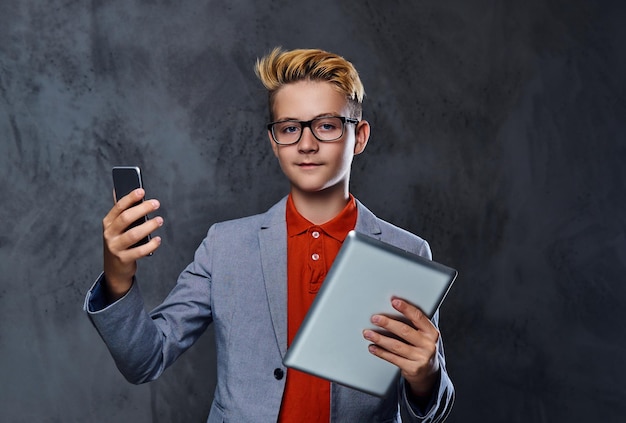 Бесплатное фото Белокурый подросток в очках держит планшетный пк и смартфон.