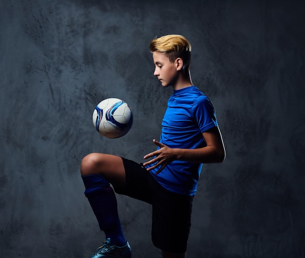 Бесплатное фото Блондинка-подросток, футболист, одетый в синюю форму, играет с мячом.