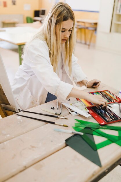 Blonde young woman choosing colored pencil from the box