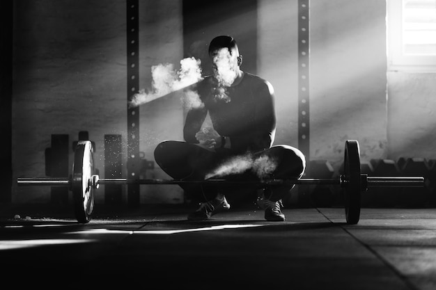 Free photo black and white photo of muscular build man using sports chalk while before lifting a barbell on weight training in a gym
