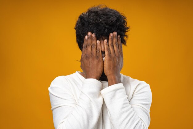 Black man closing face with hands against yellow background