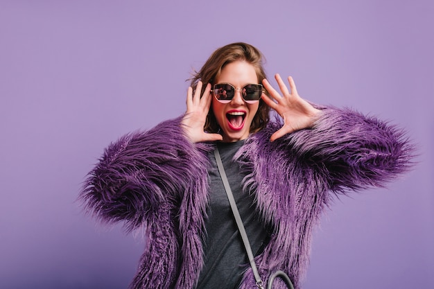 Бесплатное фото Блаженная женщина в сером наряде и фиолетовом пиджаке развлекается на фотосессии в помещении