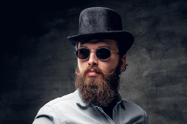 Бесплатное фото Жестокий современный мужчина в ретро солнцезащитных очках и шляпе позирует в фотостудии.