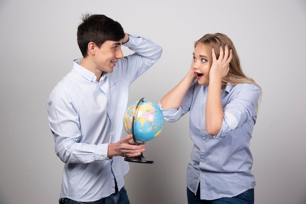 Free photo brunette guy with earth globe looking at blonde woman