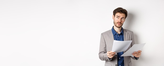 Бесплатное фото Бизнесмен в костюме просматривает бумаги, читает документы на работе и думает, глядя в сторону
